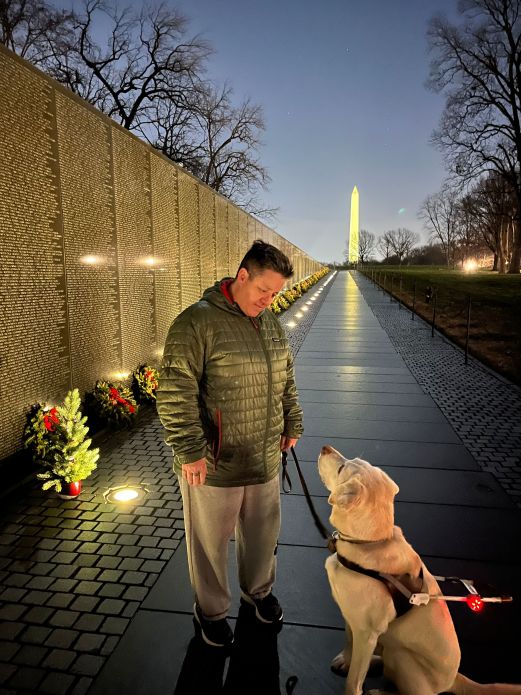 Cheri Owen with guide dog Martinez at night by the Vietnam Veterans Memorial, Washington Monument in the distance.