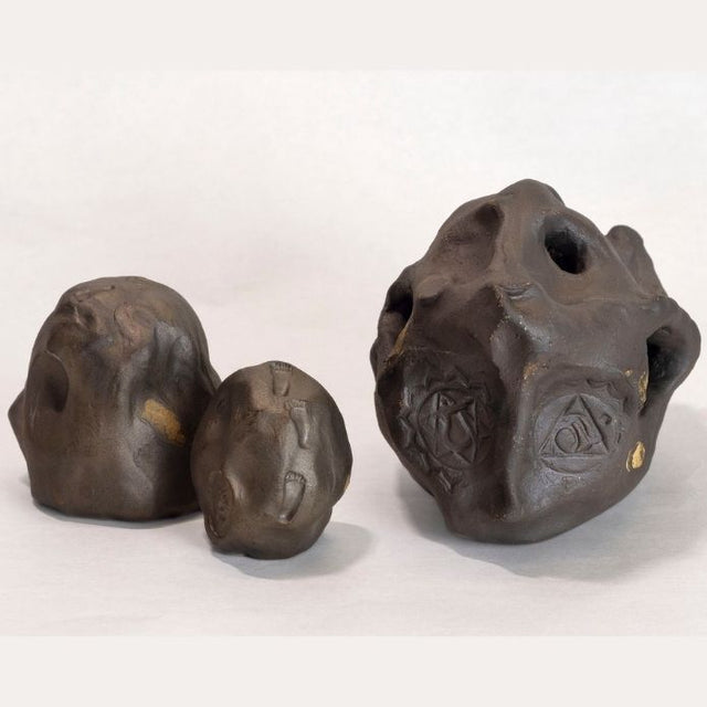 Dark brown ceramic sculpture with holes and gold accents. 