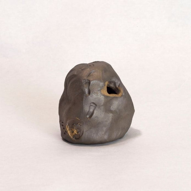 Dark brown ceramic sculpture with holes and gold accents. 