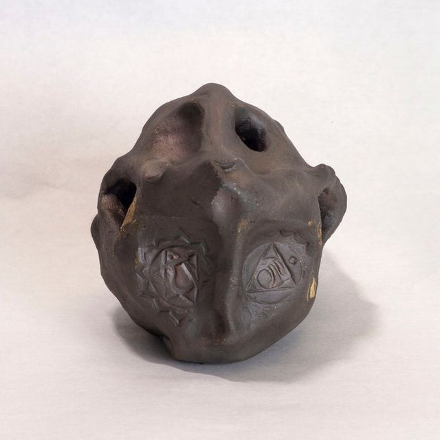 Dark brown ceramic sculpture with holes and gold accents. 