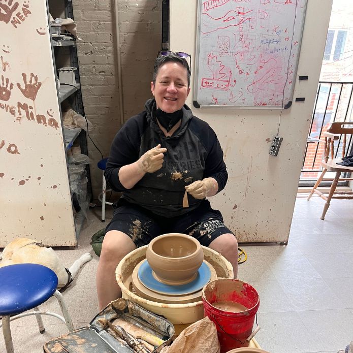 Cheri Owen smiling while shaping clay bowls on a pottery wheel in her studio.