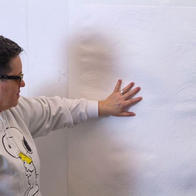 Cheri placing her hand on a raised tactile artwork of a house and landscape.