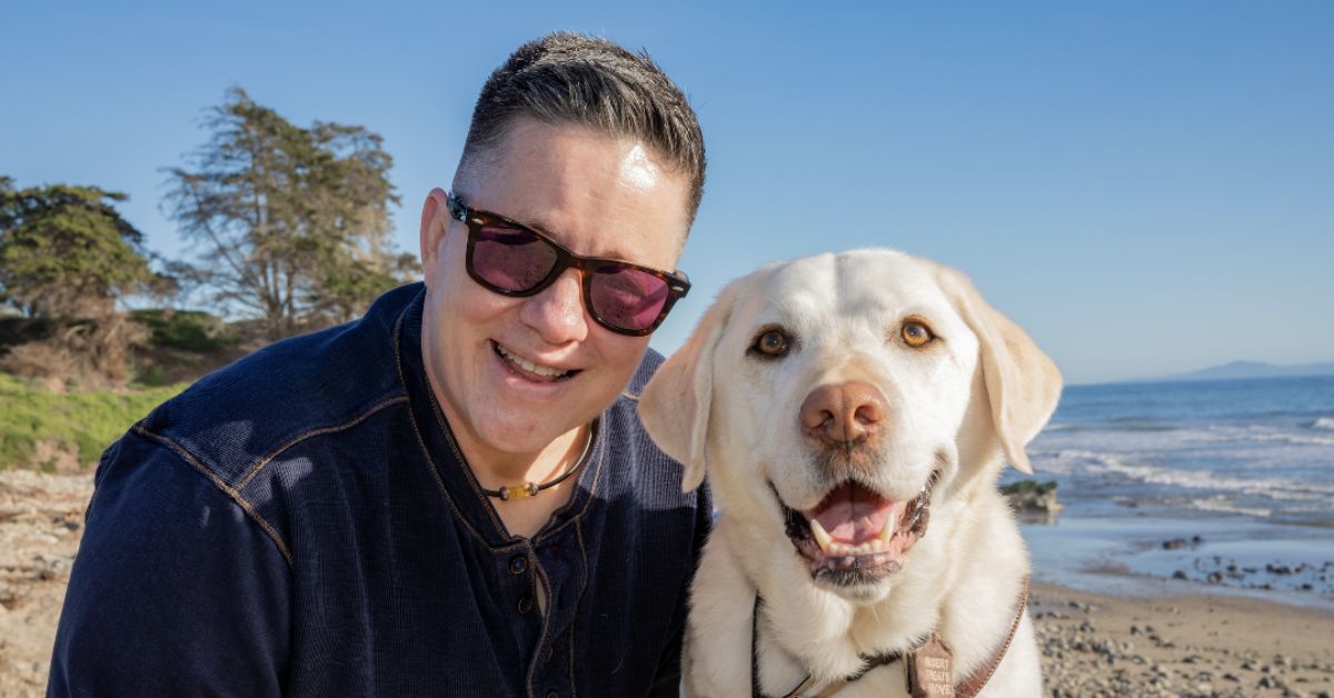 Cheri Owen and her guide dog Martinez smiling on the beach.