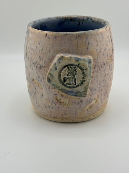 Handcrafted ceramic cup with blue-speckled glaze and a tactile Hearing the Light logo stamped on the front.