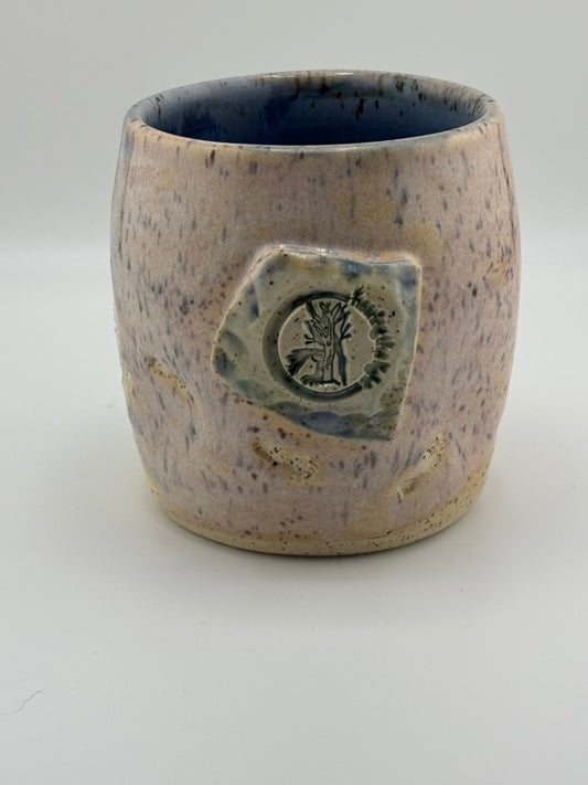 Handcrafted ceramic cup with blue-speckled glaze and a tactile Hearing the Light logo stamped on the front.