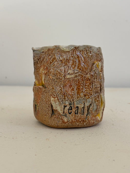 A handmade ceramic cup with a rustic, textured brown and beige glaze, featuring the word 'ready' hand-painted on the front, set against a plain light background.