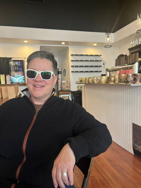 Person wearing sunglasses in a casual setting with a counter and shelves in the background