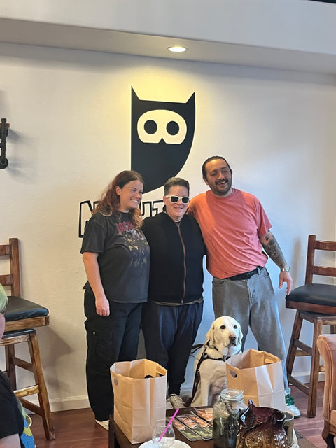 Three people smiling in front of Night Owl logo with guide dog sitting at their feet.