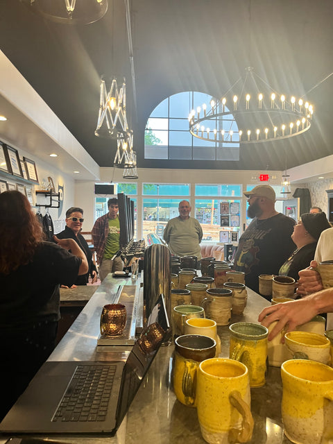 Guests gathered around counter with ceramic mugs on display at Night Owl Opening event.