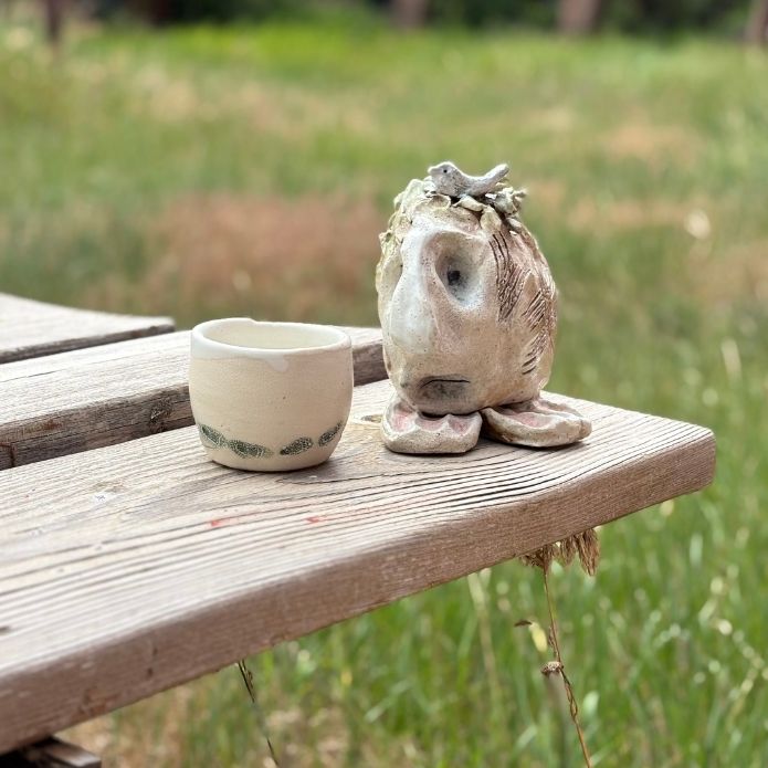 You are Safe Sculpture with porcelain mug on a wooden table with greenery background. 