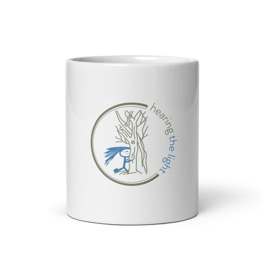 White mug with a tree and person illustration and 'hearing the light' text on a white background